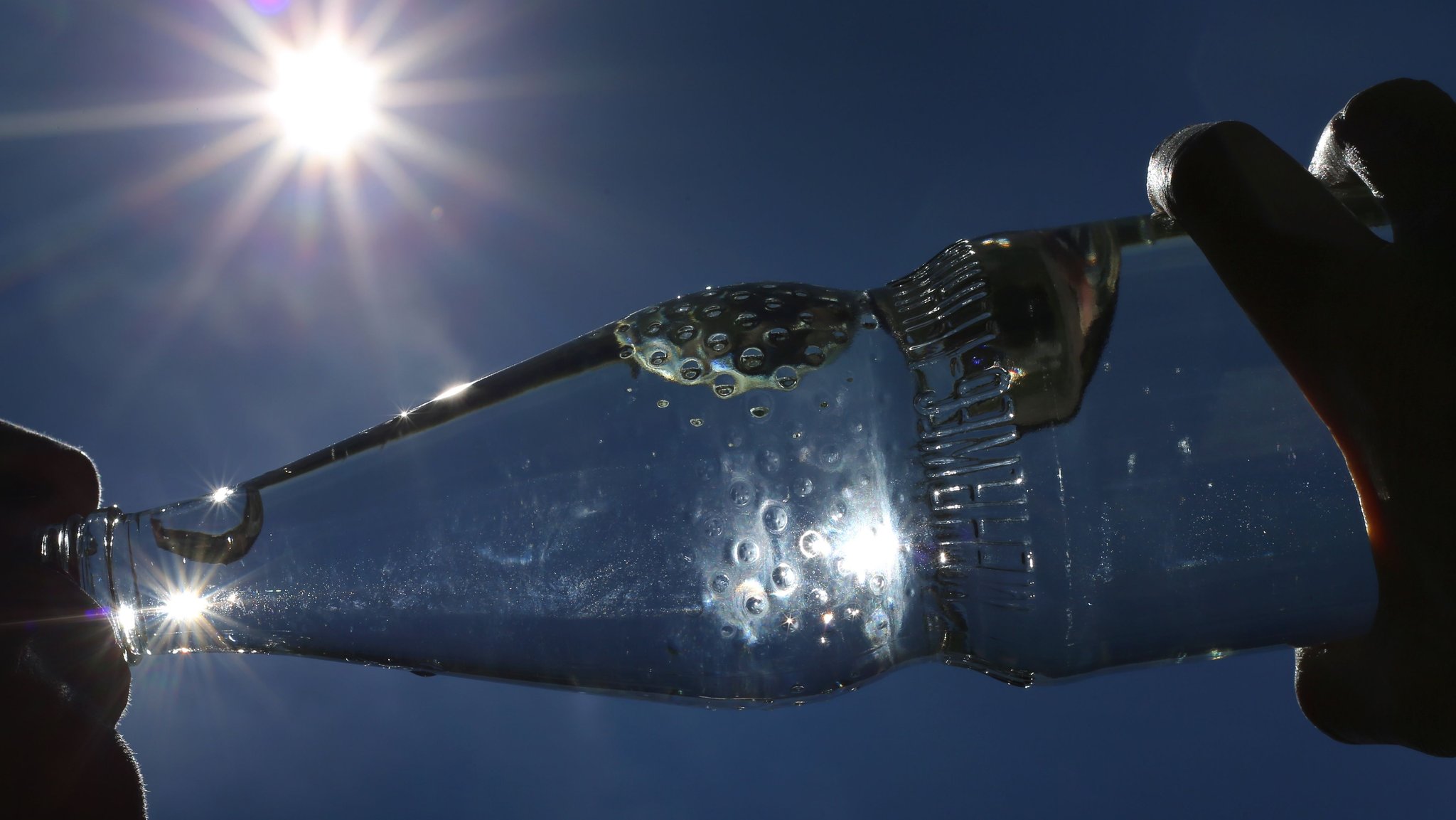 Eine Frau trinkt im Sonnenschein aus einer Flasche sprudelndes Mineralwasser. 