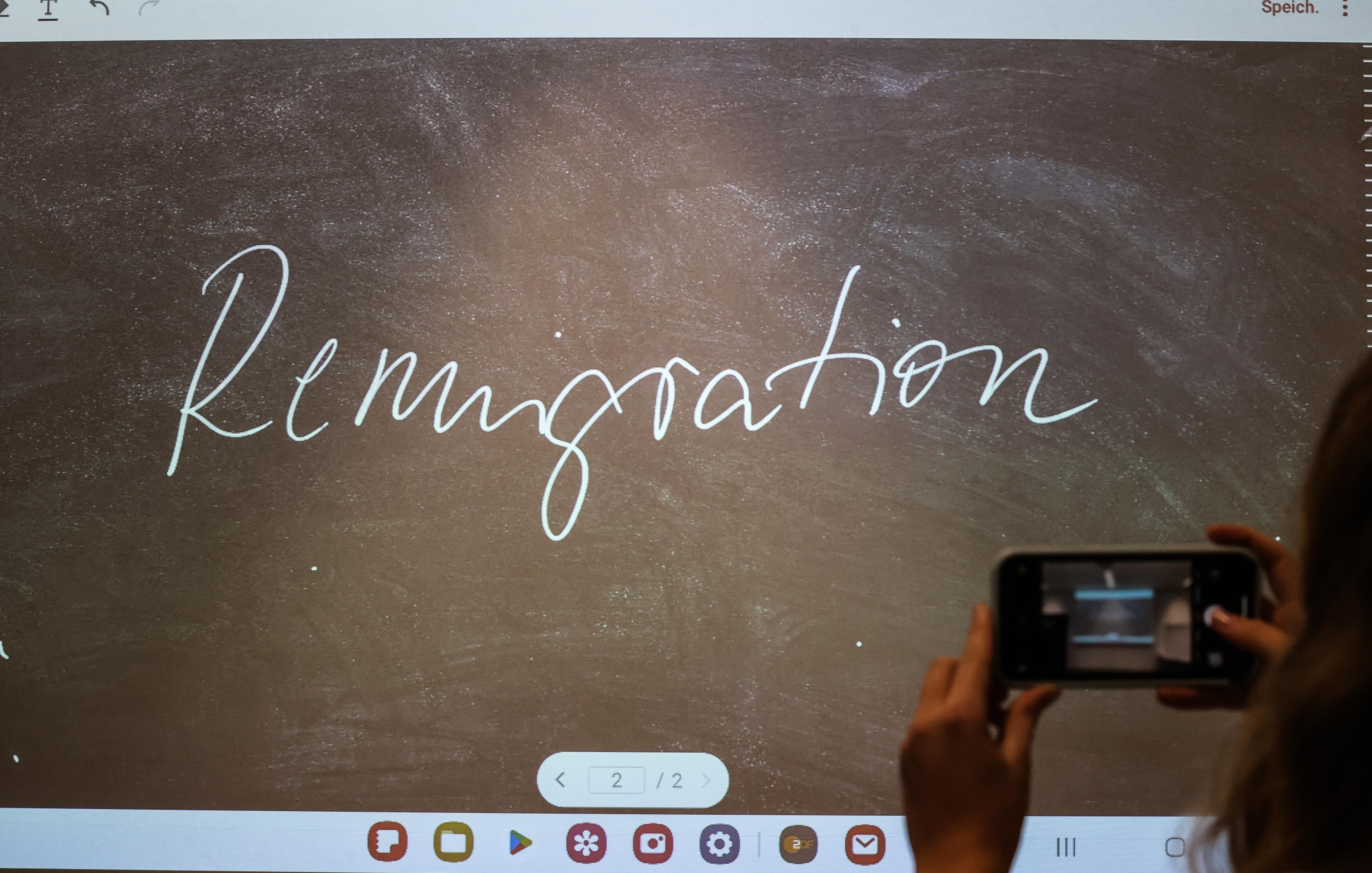 Der Begriff "Remigration" steht bei der Bekanntgabe des "Unwort des Jahres" 2023 auf einem Bildschirm und wird mit einem Smartphone fotografiert.