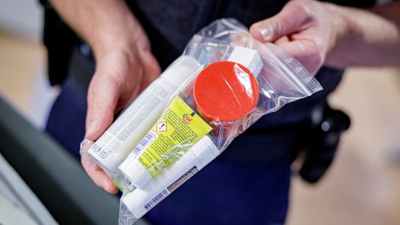 Ein Beamter der Bundespolizei zeigt beim Sicherheitscheck welche Flüssigkeitsmengen mitgeführt werden dürfen und wie sie verpackt sein müssen. | Bild: picture alliance/dpa | Axel Heimken Ein Beamter der Bundespolizei zeigt beim Sicherheitscheck welche Flüssigkeitsmengen mitgeführt werden dürfen und wie sie verpackt sein müssen.