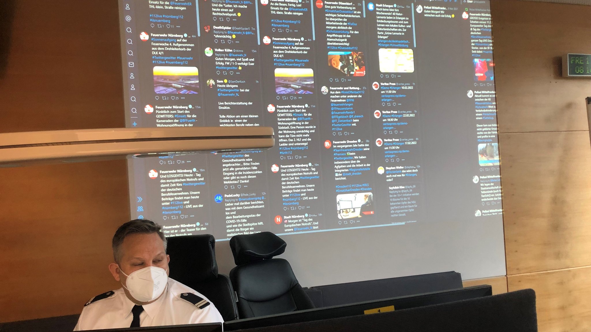 In der ILS Nürnberg: Tweetdeck auf einer Leinwand, davor ein Feuerwehrmann vor seinen Bildschirmen. 