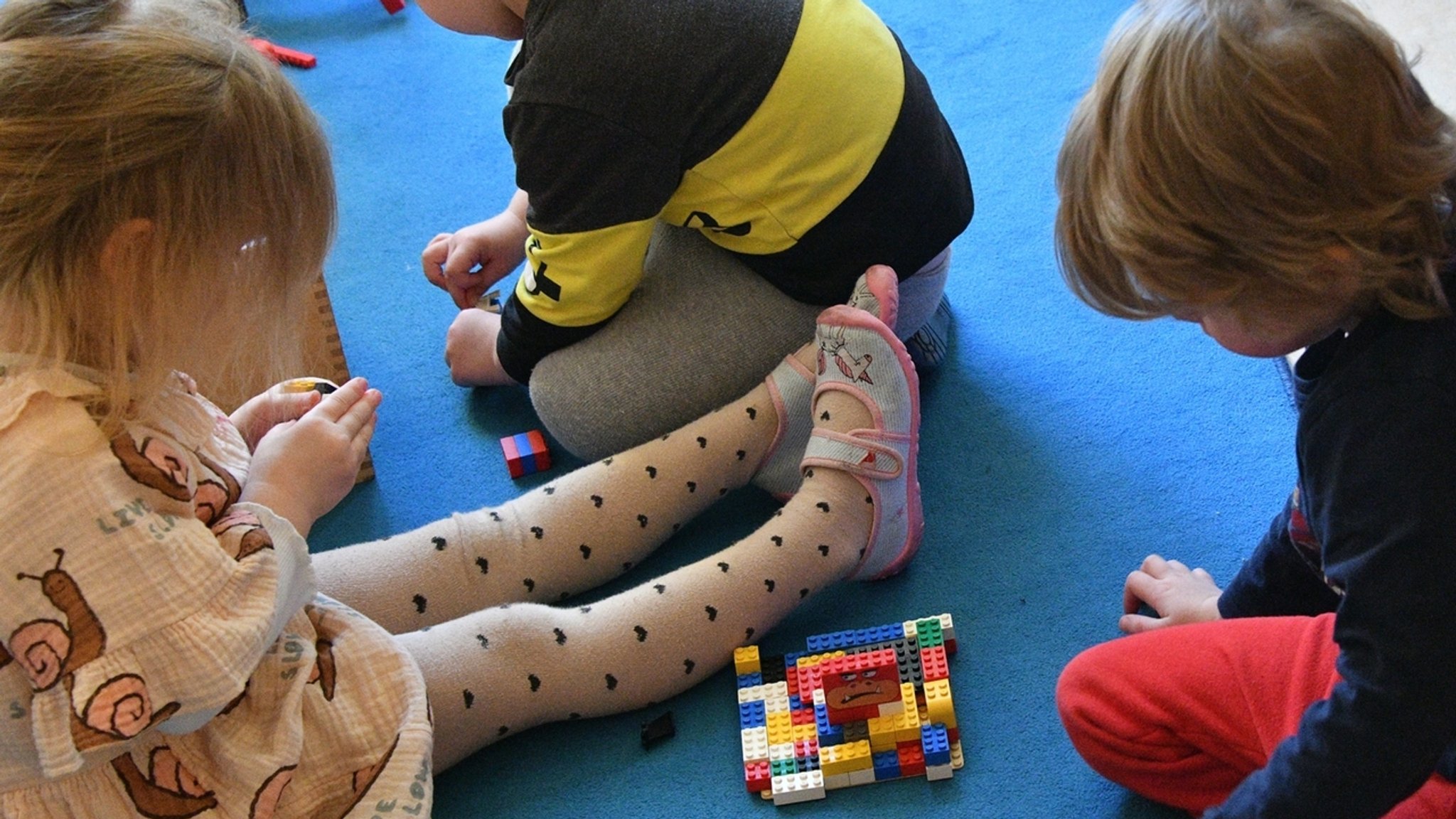 Kinder sitzen in einer Kita auf dem Boden und spielen mit Lego-Bausteinen