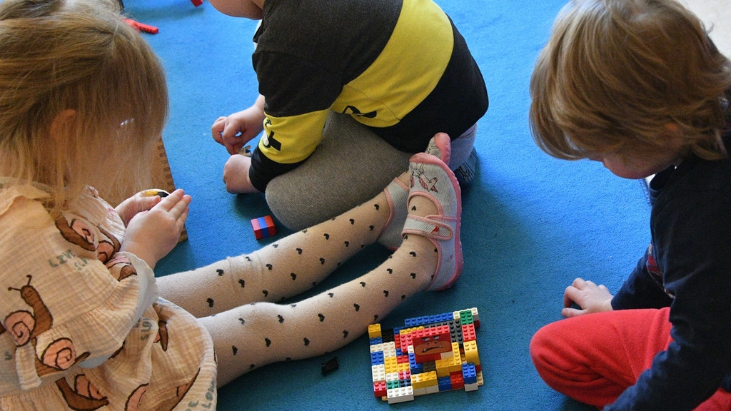 Kinder sitzen in einer Kita auf dem Boden und spielen mit Lego-Bausteinen