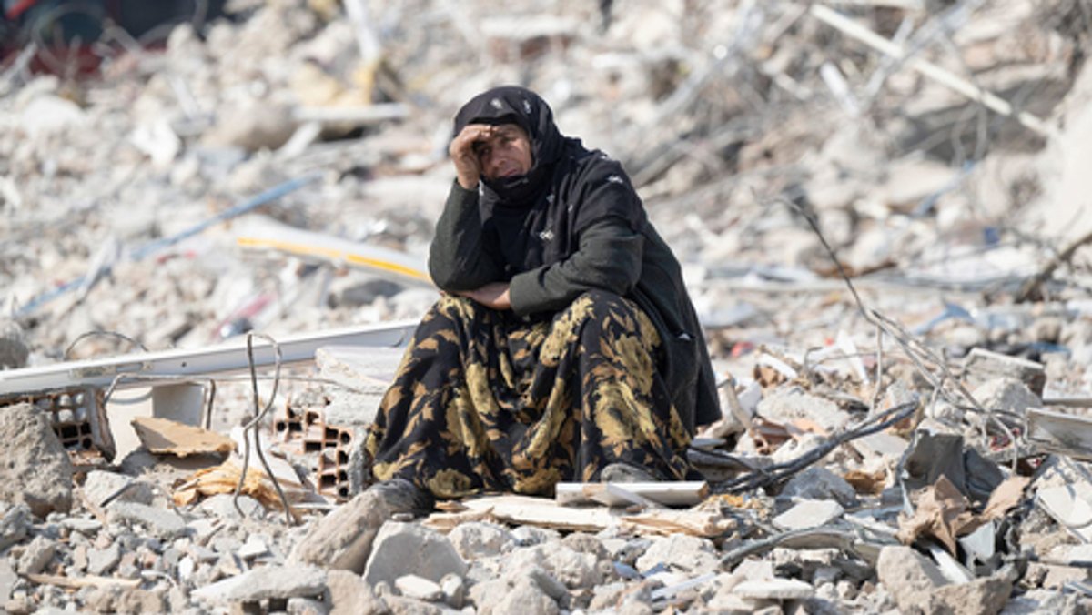 Eine Frau sitzt nach den verherrenden Beben in der Türkei zwischen Trümmern, alles um sie herum ist zerstört.