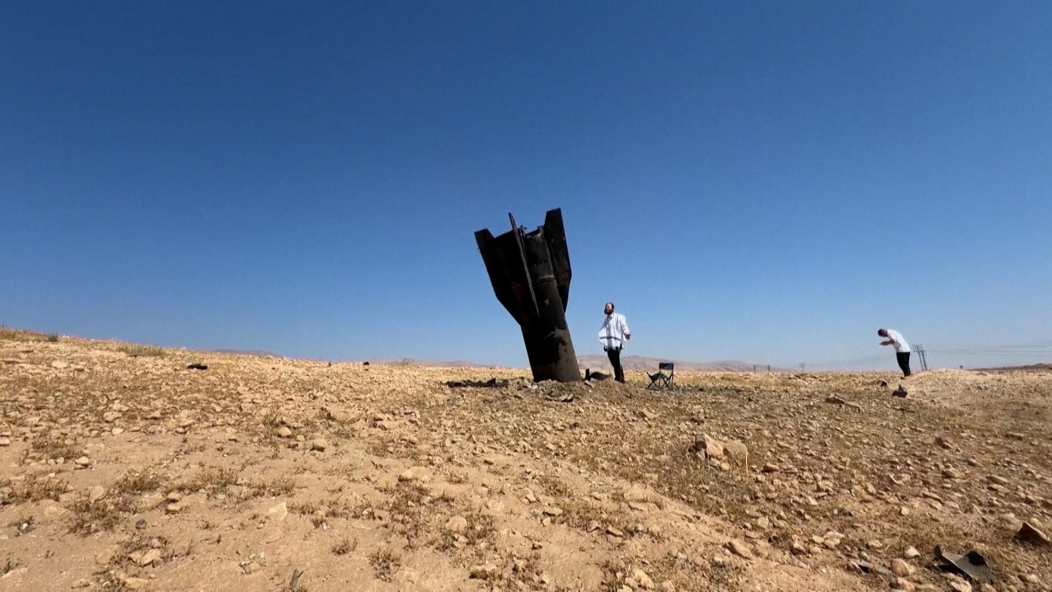 Ein Mann steht neben den Überresten einer iranischen Rakete, die in der Nähe von Jericho, einer Stadt im Palästinensischen Autonomiegebiet am Westufer des Jordans eingeschlagen war. | Bild: Screenshot/Reuters Ein Mann steht neben den Überresten einer iranischen Rakete, die in der Nähe von Jericho, einer Stadt im Palästinensischen Autonomiegebiet am Westufer des Jordans eingeschlagen war.