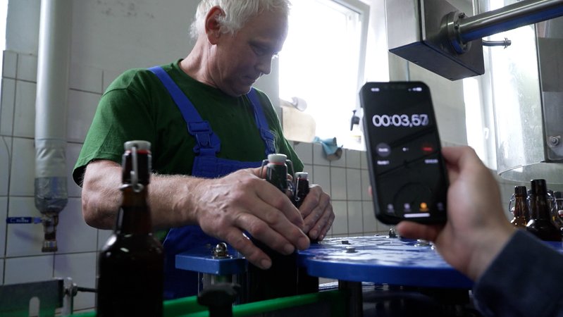 Mann schließt an einem Förderband Bügelbierflaschen mit der Hand. | Bild: BR24 Mann schließt an einem Förderband Bügelbierflaschen mit der Hand.