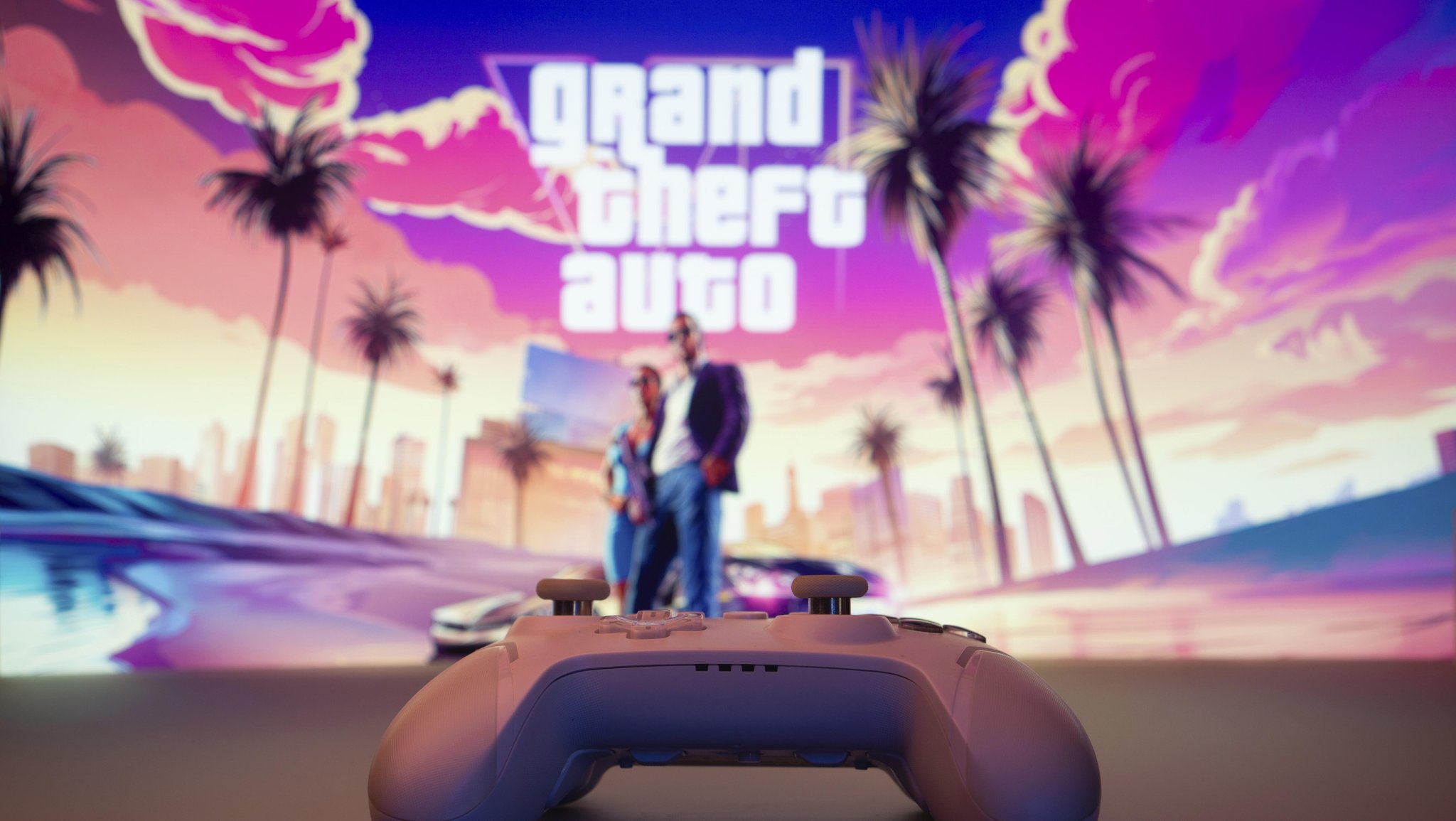 Eine Nahaufnahme eines weißen Gamepads mit Grand Theft Auto VI auf dem Bildschirm im Hintergrund.