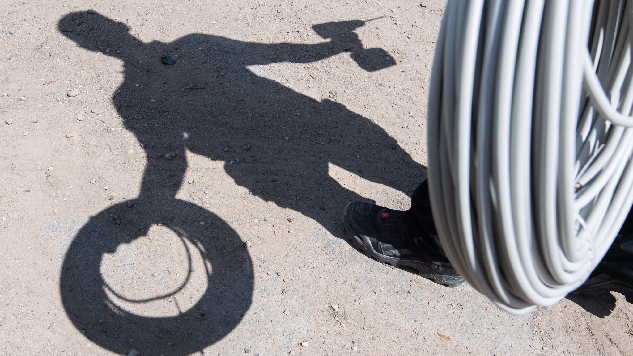 Der Schatten eines Mannes auf dem Boden, der eine Kabelrolle und einen Akkuschrauber in den Händen hält. (Symbolbild)