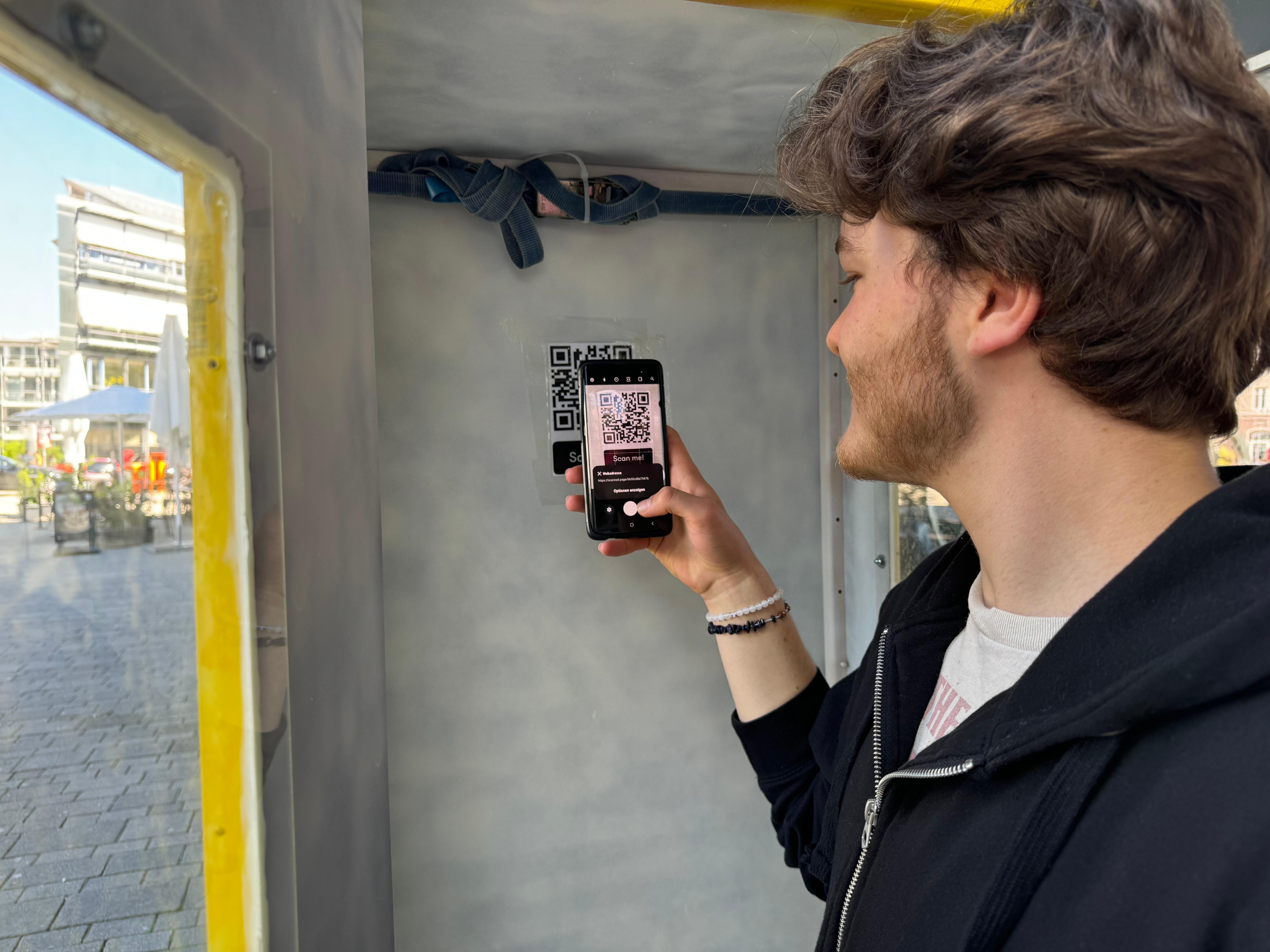 Ein Jugendlicher steht in einer Telefonzelle und scannt einen QR-Code.
