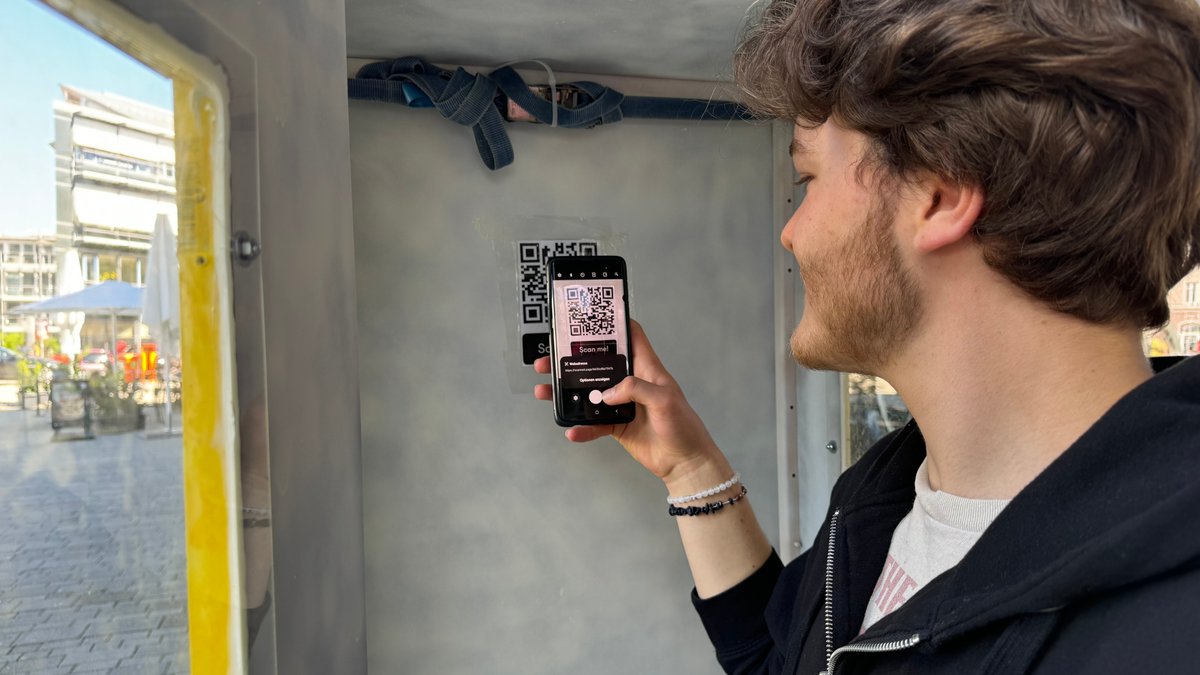 Ein Jugendlicher scannt einen QR-Code und steht in einer Telefonzelle