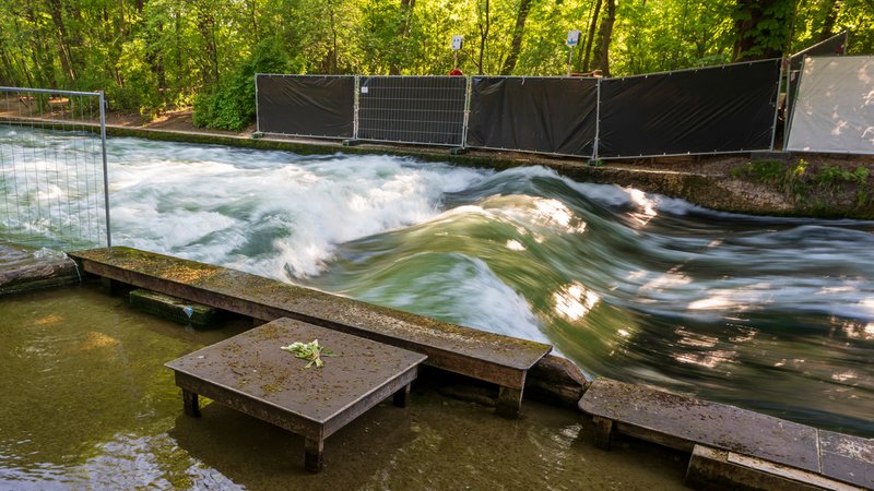 Ein Blumenstrauss liegt hinter einem Absperrzaun am Ufer der künstliche Eisbachwelle im Englischen Garten. | Bild: picture alliance/dpa | Peter Kneffel Ein Blumenstrauss liegt hinter einem Absperrzaun am Ufer der künstliche Eisbachwelle im Englischen Garten.