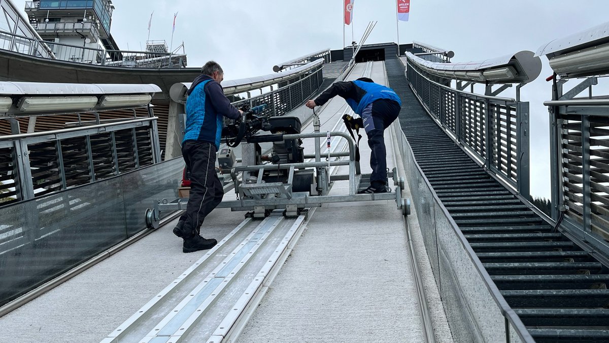 Zwei Männer präparieren die Skisprungschanzen; der BR hat sie mit der Kamera begleitet.
