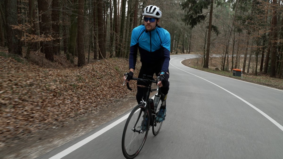 Maxi Schwarzhuber fährt auf dem Rad eine ansteigende Straße hoch, die durch einen Wald führt.