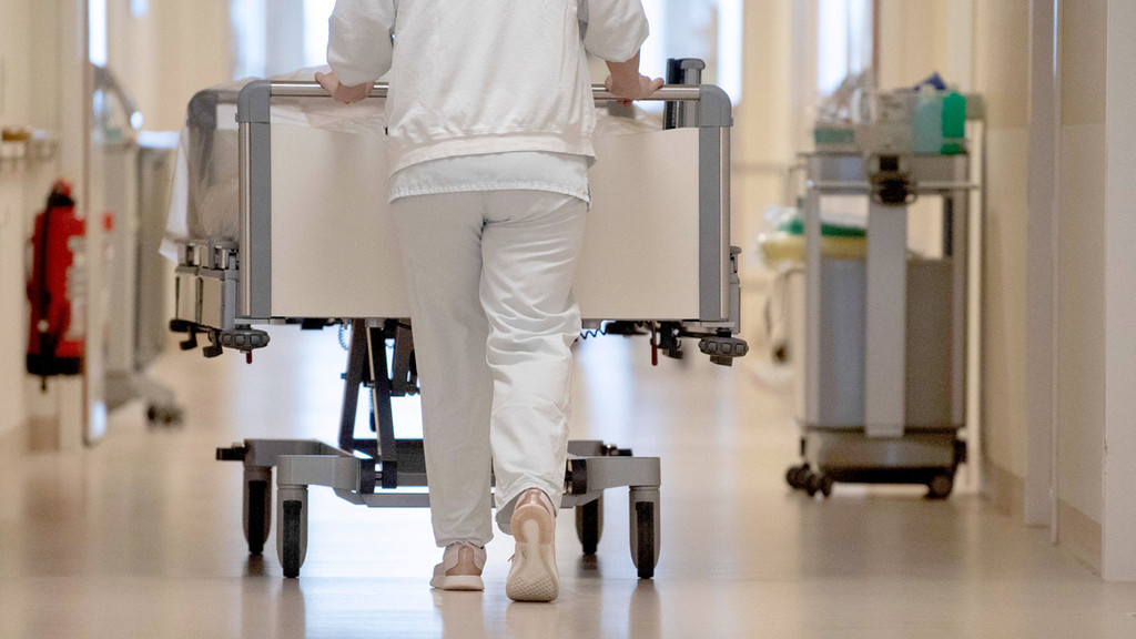 Eine Krankenpflegerin schiebt ein Krankenbett durch einen Krankenhausflur.