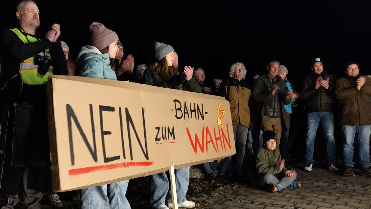 Teilnehmer einer Kundgebung gegen die geplante Bahn-Trasse bei Adelsried mit Transparent "Nein zum Bahn-Wahn"