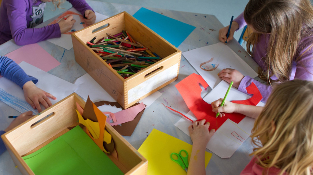 Grundschülerinnen sitzen an einem Tisch in einem Kinderhort und malen und basteln.