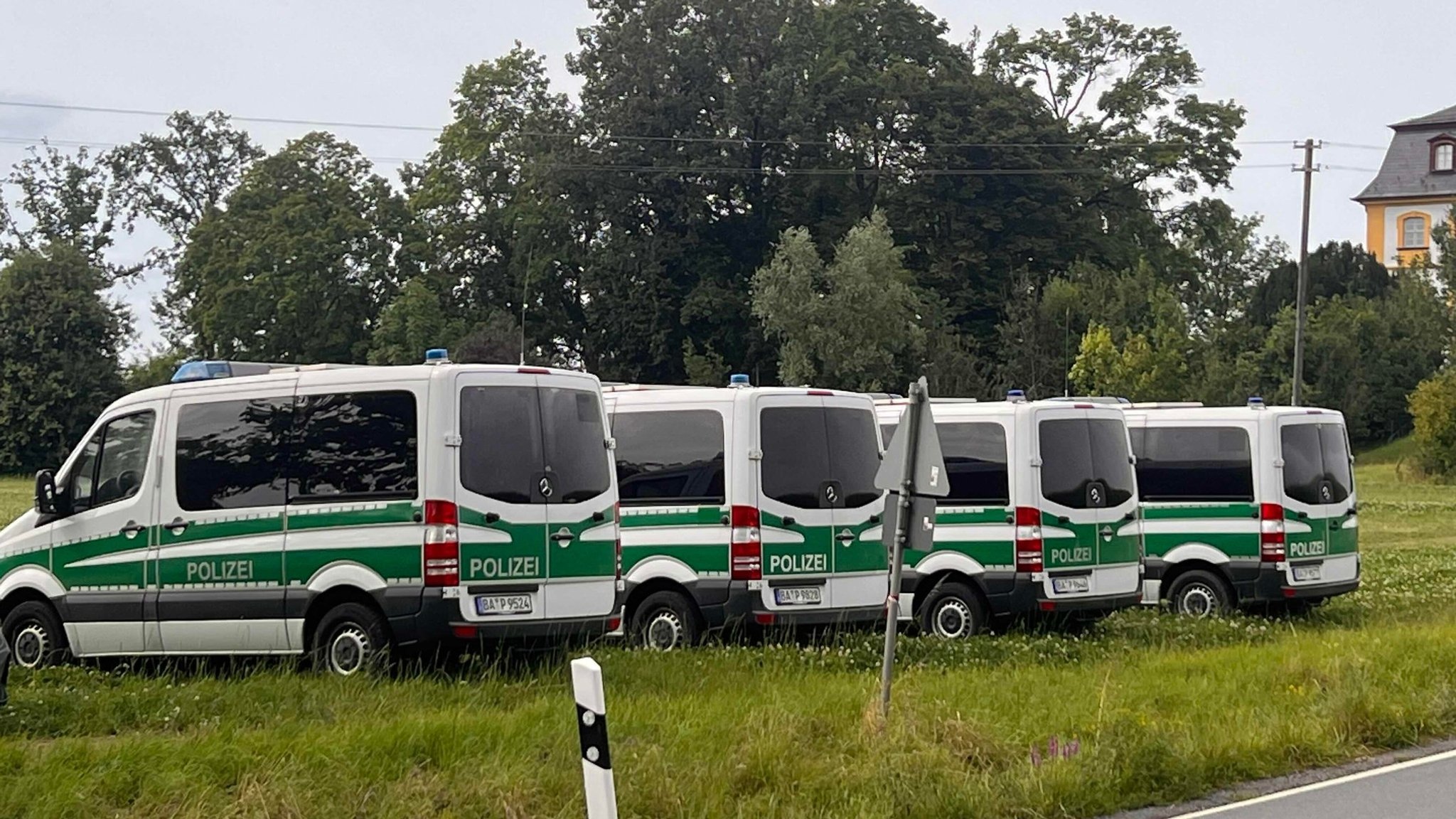 Vier Einsatzfahrzeuge der Polizei stehen auf einer Wiese neben einer Straße.