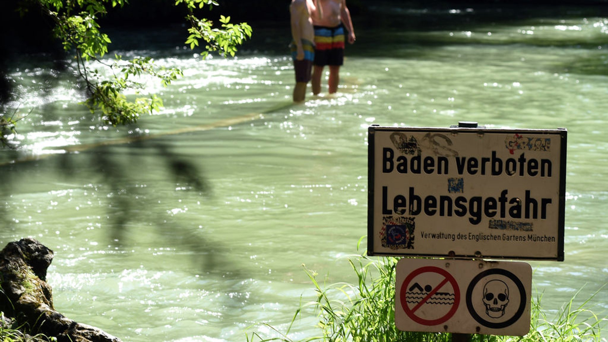 ARCHIV - 06.06.2015, Bayern, München: Ein Schild mit der Aufschrift «Baden verboten Lebensgefahr» steht am 07.06.2015 am Ufer des Eisbachs im Englischen Garten in München (Bayern). Warme Temperaturen und blauer Himmel bestimmen das Wetter in der Landeshauptstadt. Foto\ Felix Hörhager/dpa +++(c) dpa - Bildfunk+++ (zu dpa: «Polizei: Leiche im Eisbach ist wohl vermisster Student») Foto: Felix Hörhager/dpa +++ dpa-Bildfunk +++