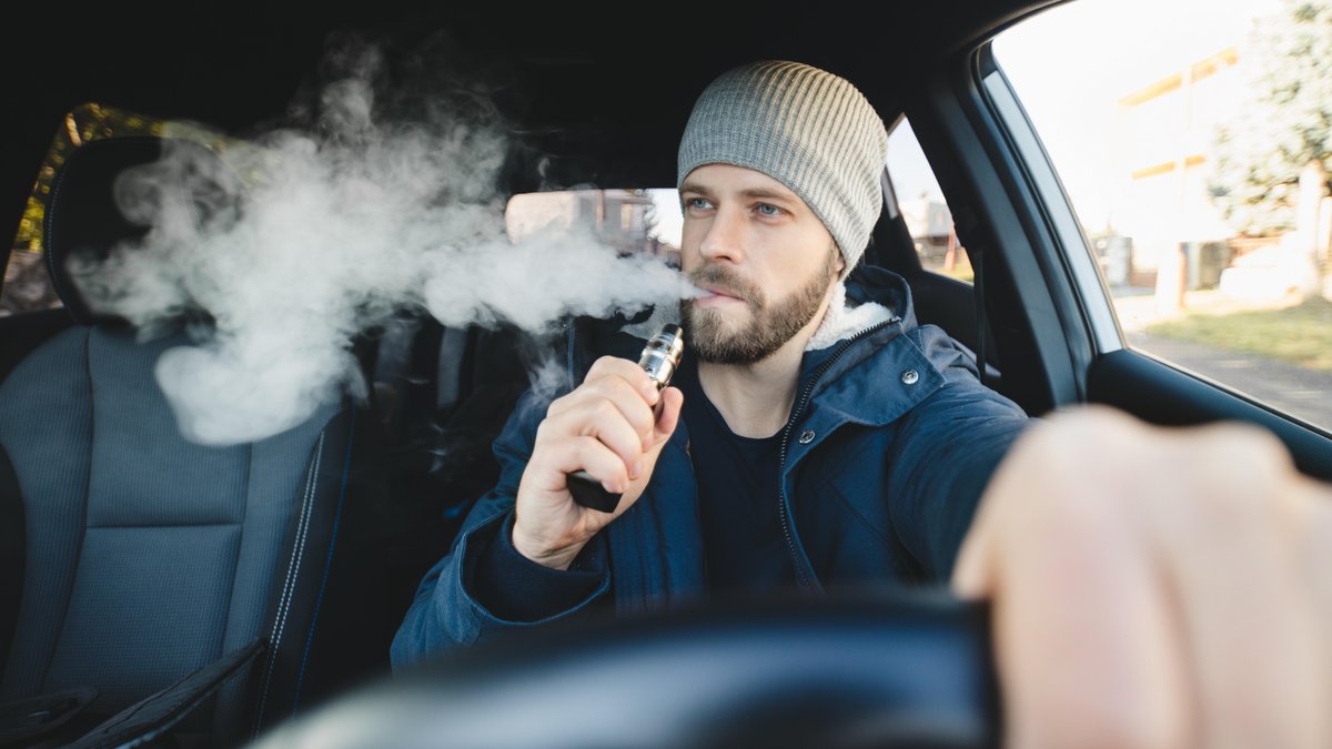 Mann raucht am Steuer seines Autos eine E-Zigarette (Symbolbild)