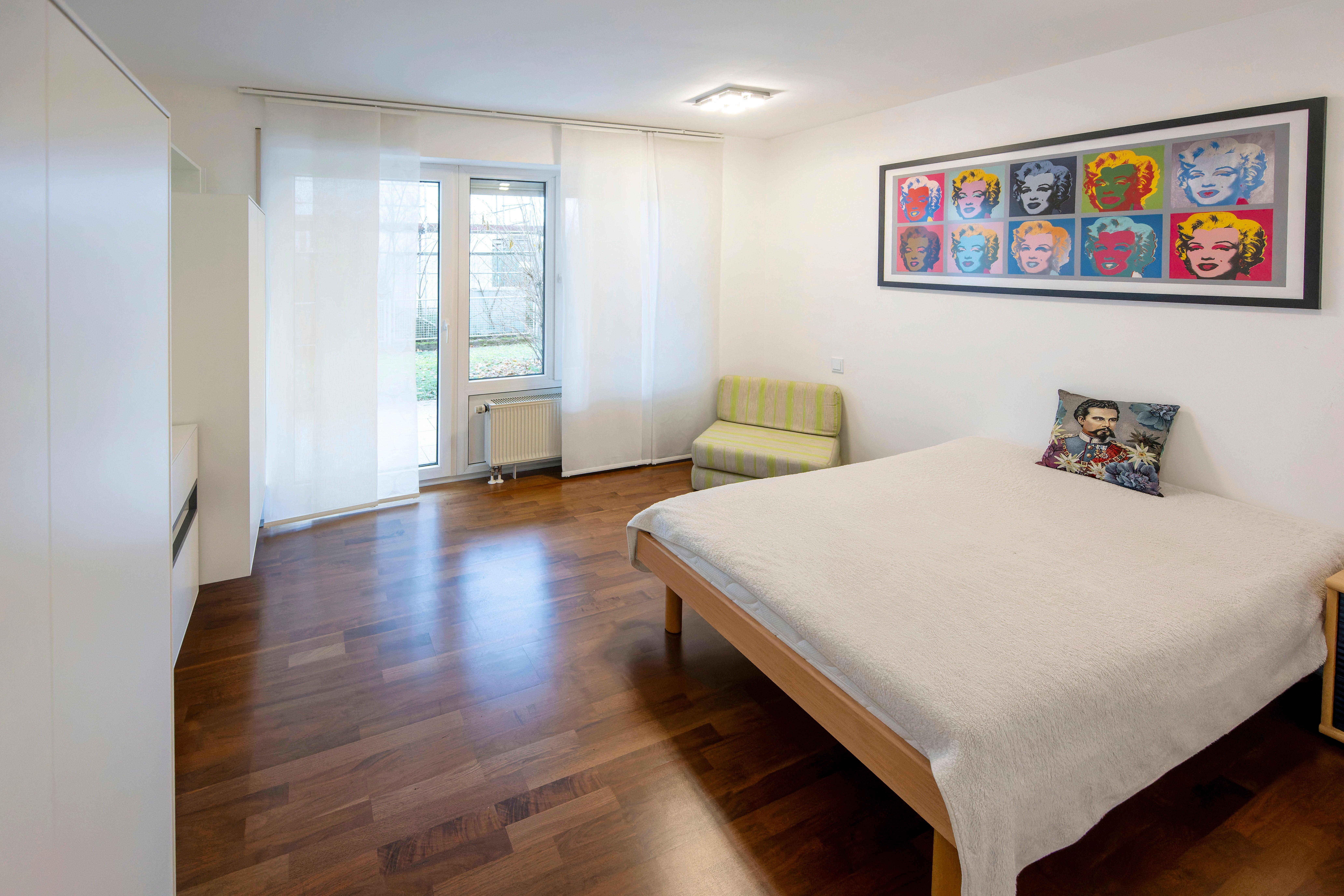 Innenansicht eines Zimmers mit einem Bett, auf dem ein Kissen mit König Ludwig Konterfei liegt.