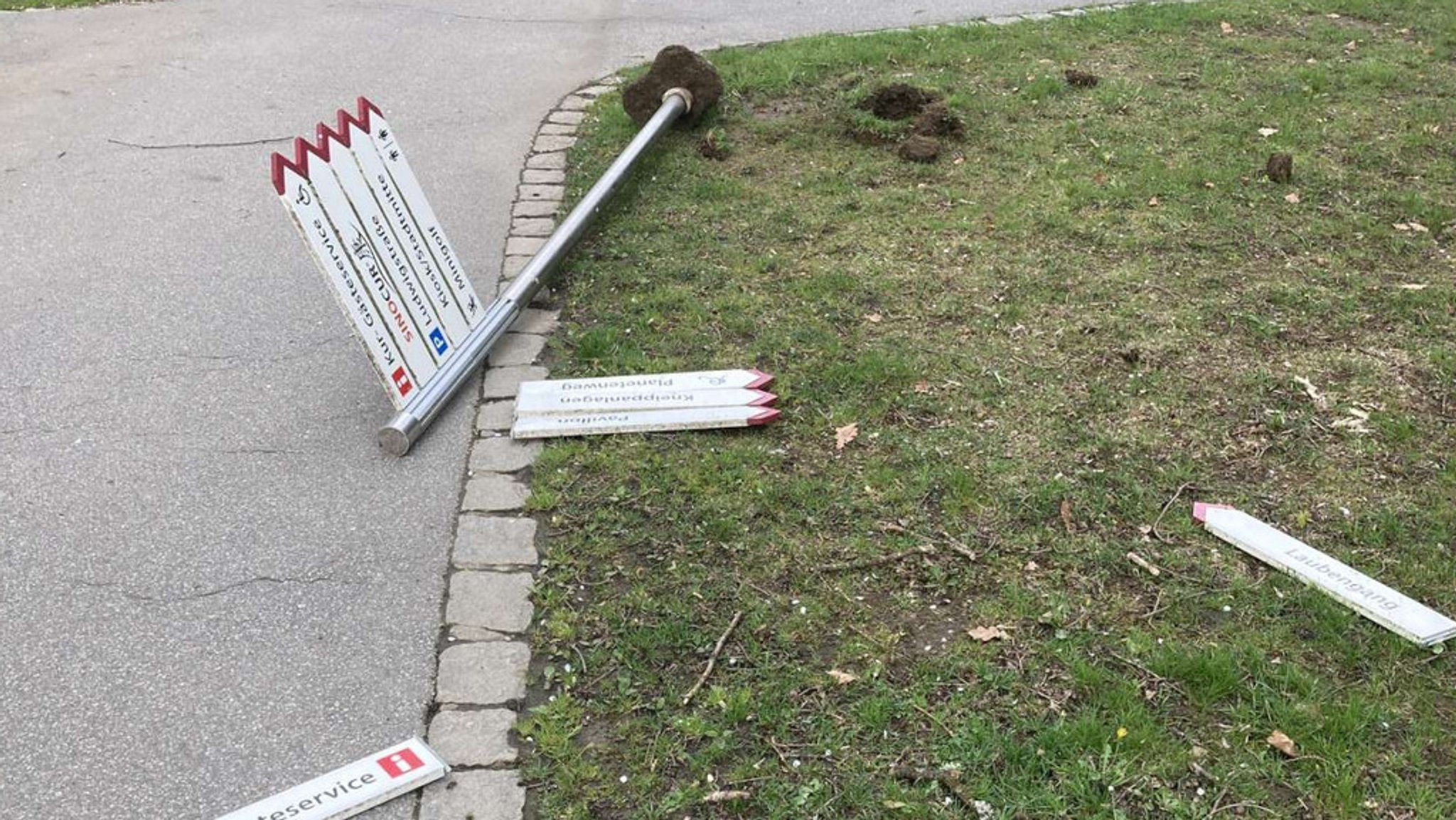 Herausgerissener Wegweiser und abgebrochene Schilder liegen am Boden.