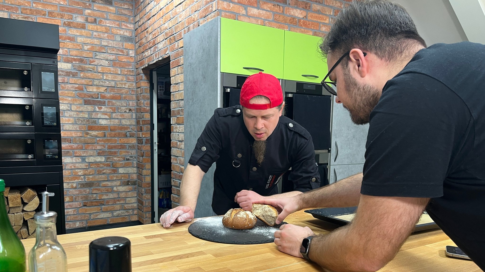 Zwei Männer legen selbstgebackenes Brot auf eine Schieferplatte. 