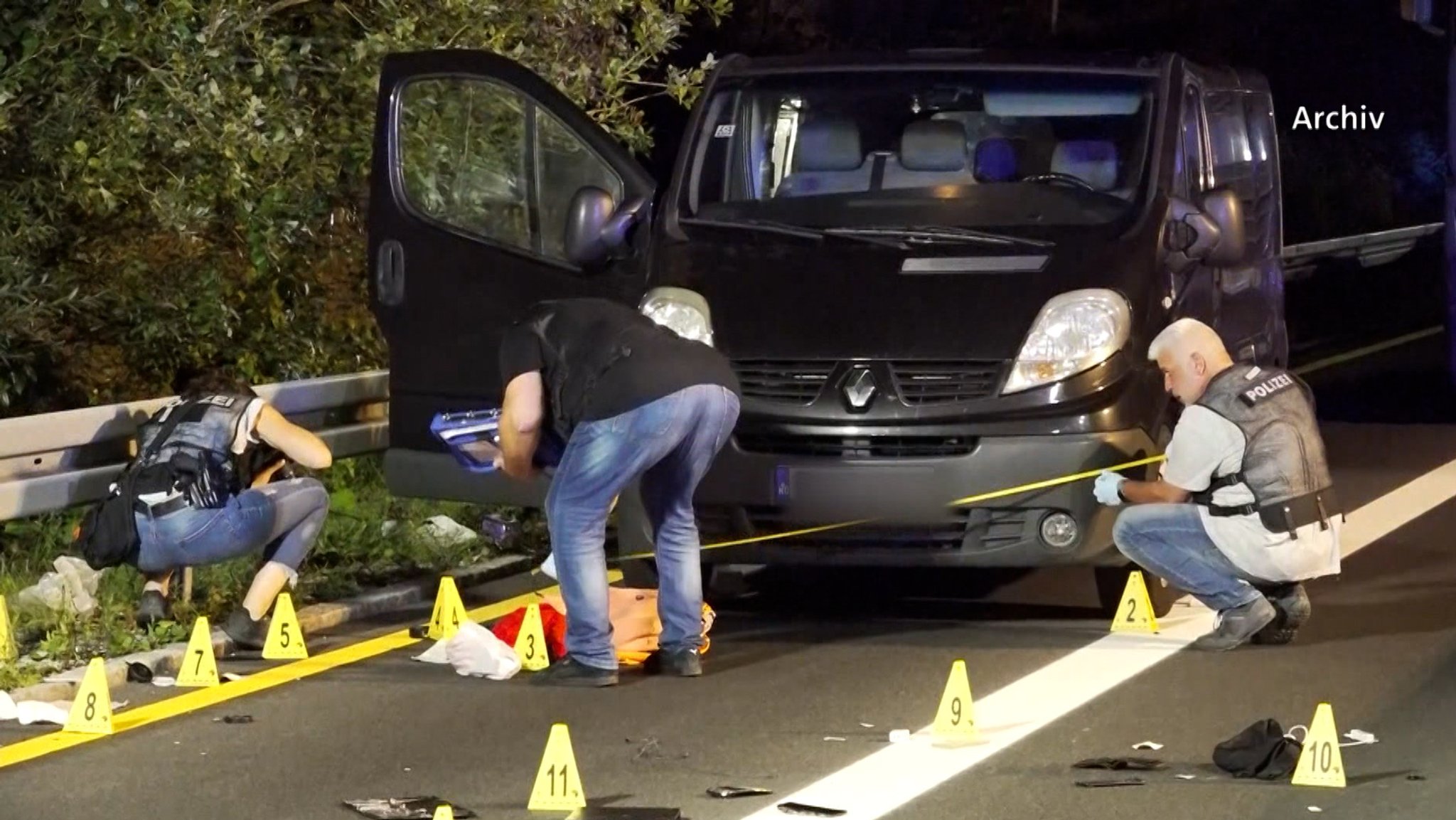 Ermittler der Polizei sichern Spuren auf einer Straße, auf der ein Kleinbus parkt. 