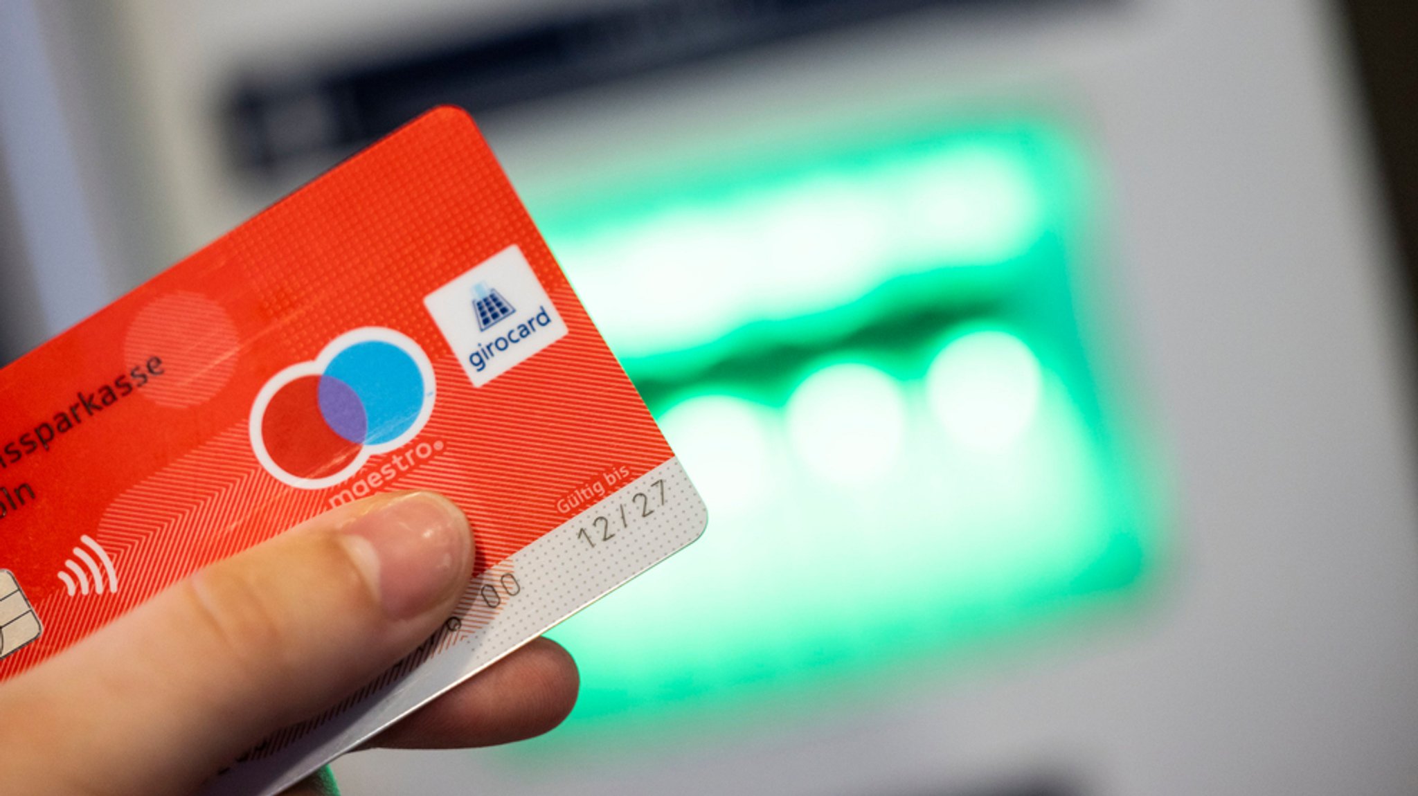 Eine Girocard mit Maestro-Logo wird vor einen Geldautomaten gehalten.