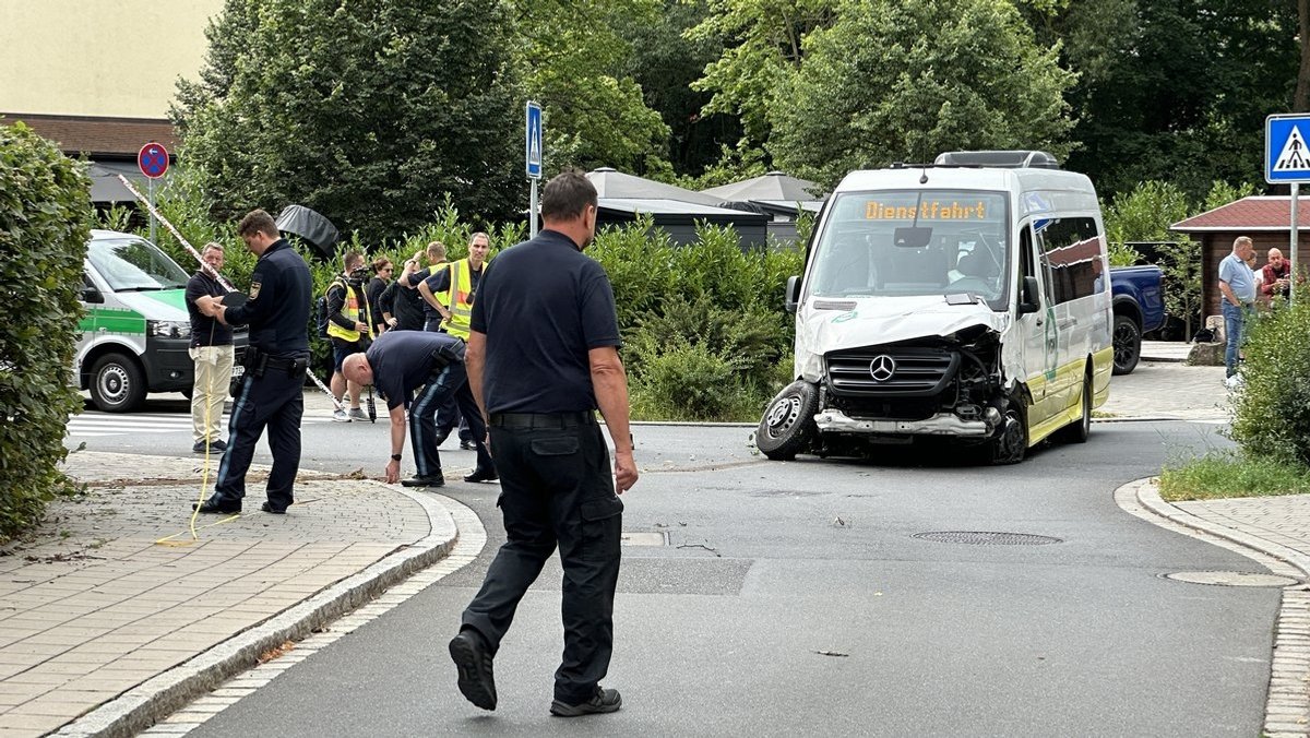 Ein zerstörter Midi-Bus steht nach einem Unfall auf einer Straße, umgeben von Polizei.