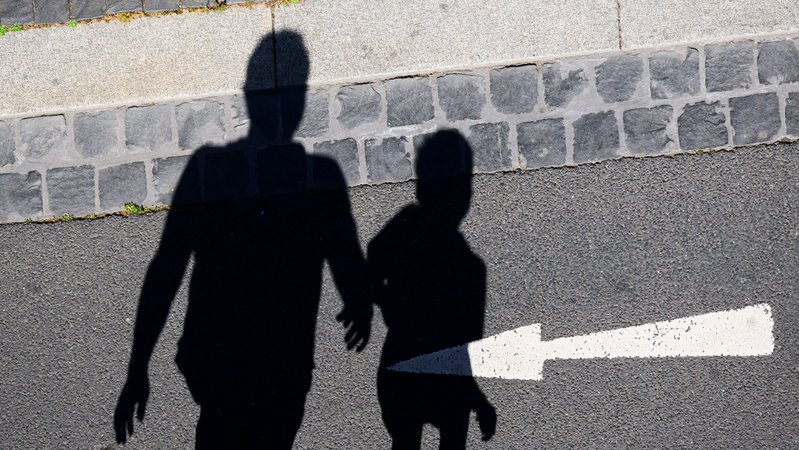 Symbolbild: Der Schatten von einem Mann und einem Kind sind auf einer Straße mit einem Pfeil zu sehen. | Bild: picture alliance /dpa | Julian Stratenschulte Symbolbild: Der Schatten von einem Mann und einem Kind sind auf einer Straße mit einem Pfeil zu sehen.