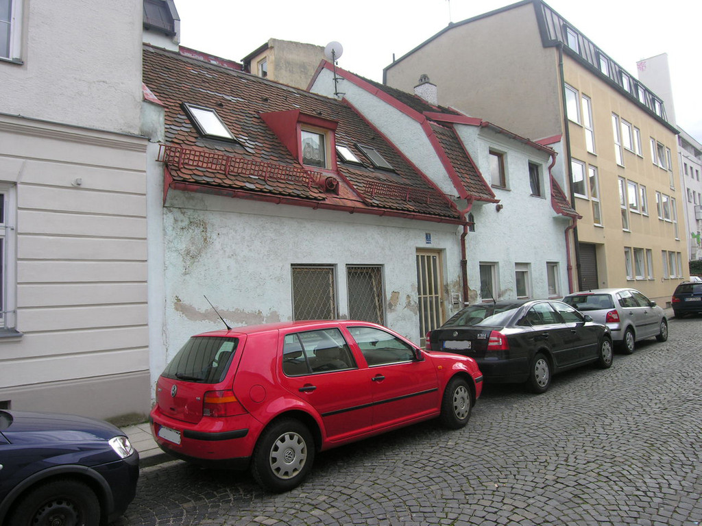 Eine Straße im Münchner Stadtteil Giesing. Ein kleines altes Haus mit steilem Ziegeldach steht zwischen höheren Gebäuden, davor parken Autos. Aufnahme von 2011.