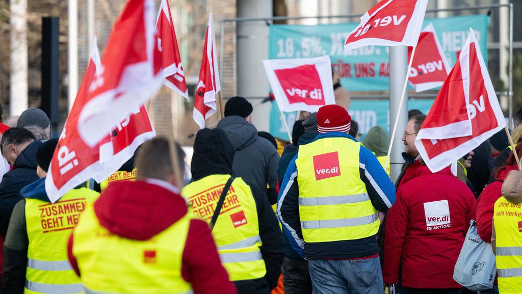 Mitglieder der Gewerkschaft Verdi demonstrieren in Warnwesten und tragen Gewerkschaftsfahnen.