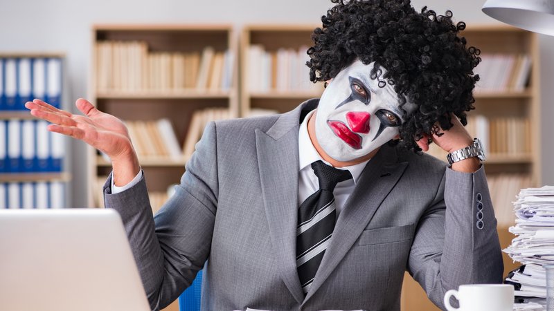 Mann im Anzug und Clownsmaske am Schreibtisch mit Laptop 