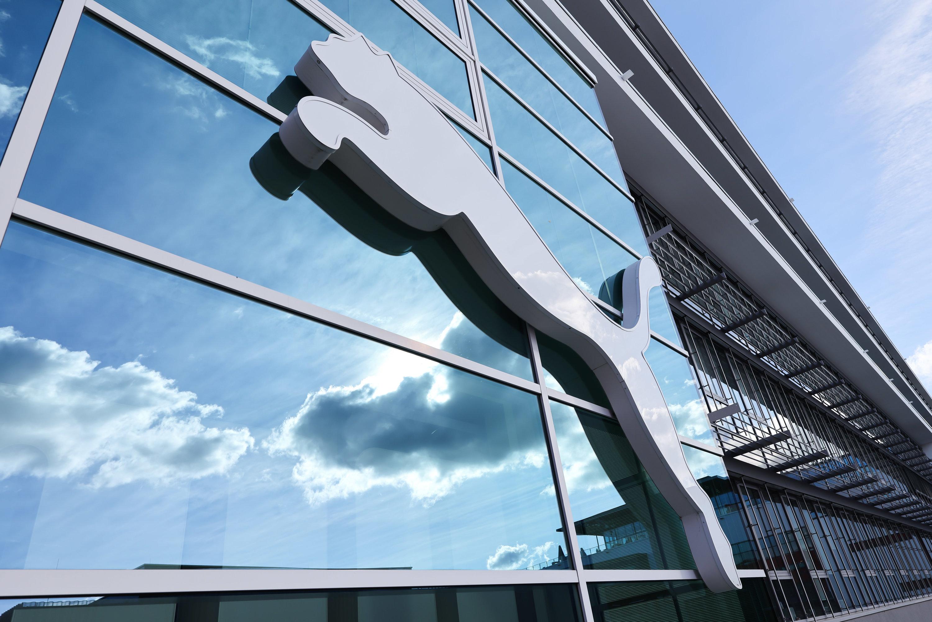 Wolken spiegeln sich im Fenster hinter einem Puma-Logo am Firmensitz des Sportartikelherstellers in Herzogenaurach