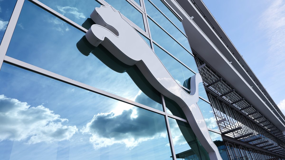 Wolken spiegeln sich im Fenster hinter einem Puma-Logo am Firmensitz des Sportartikelherstellers in Herzogenaurach