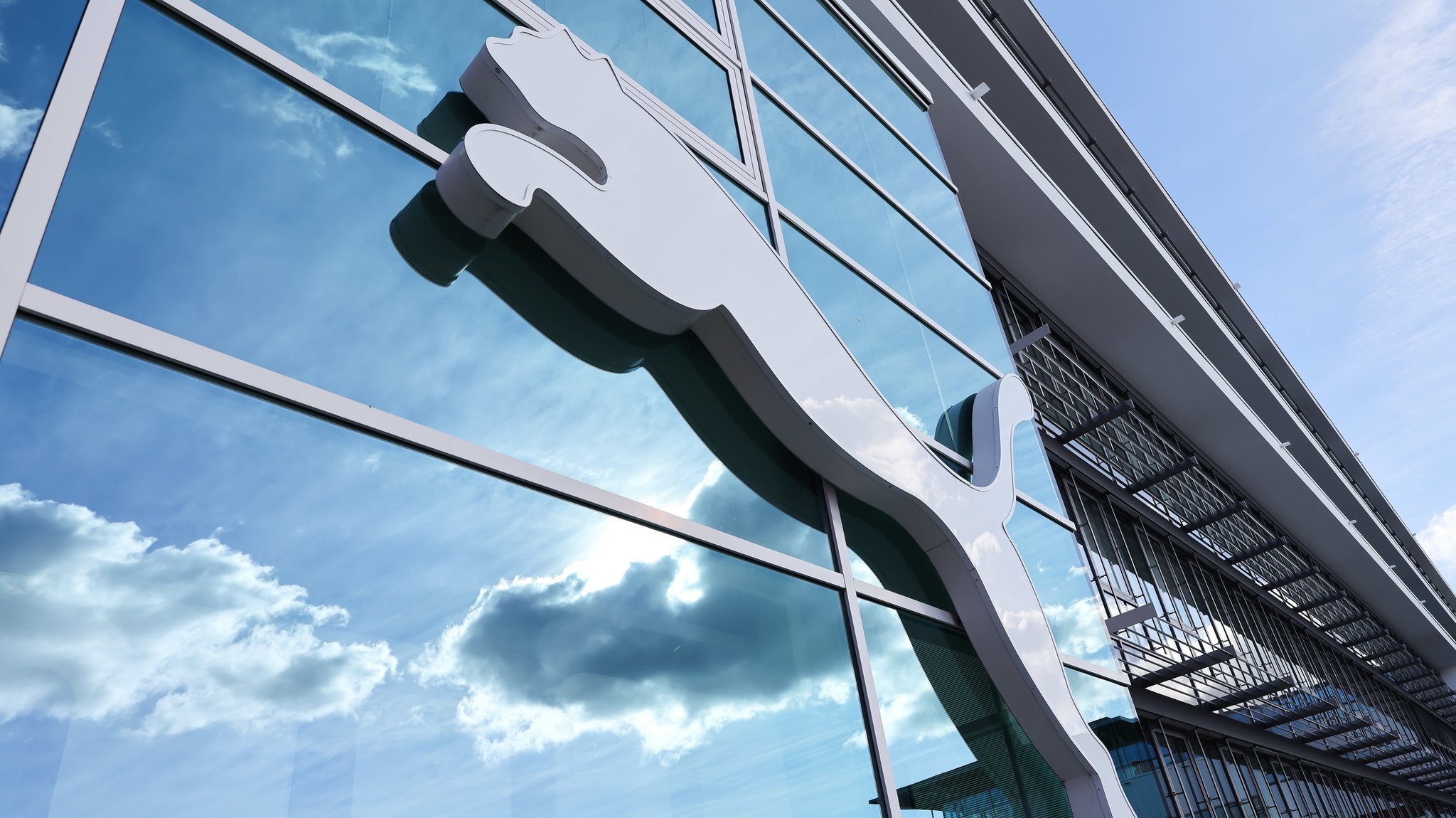 Wolken spiegeln sich im Fenster hinter einem Puma-Logo am Firmensitz des Sportartikelherstellers in Herzogenaurach