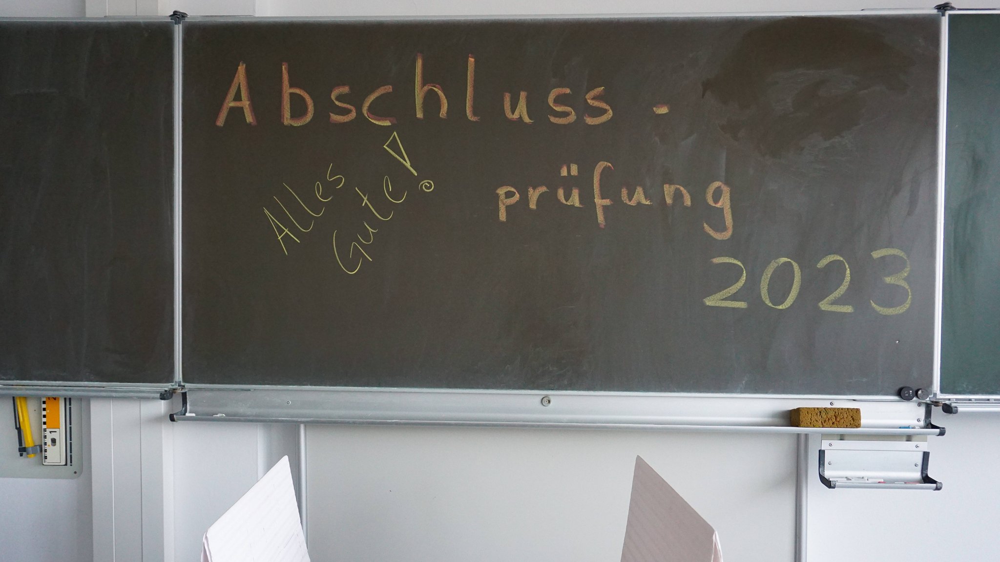 Kreidetafel einer allgemeinbildenden Schule. An der Tafel steht der Schriftzug "Abschlussprüfung 2023". "Alles Gute"