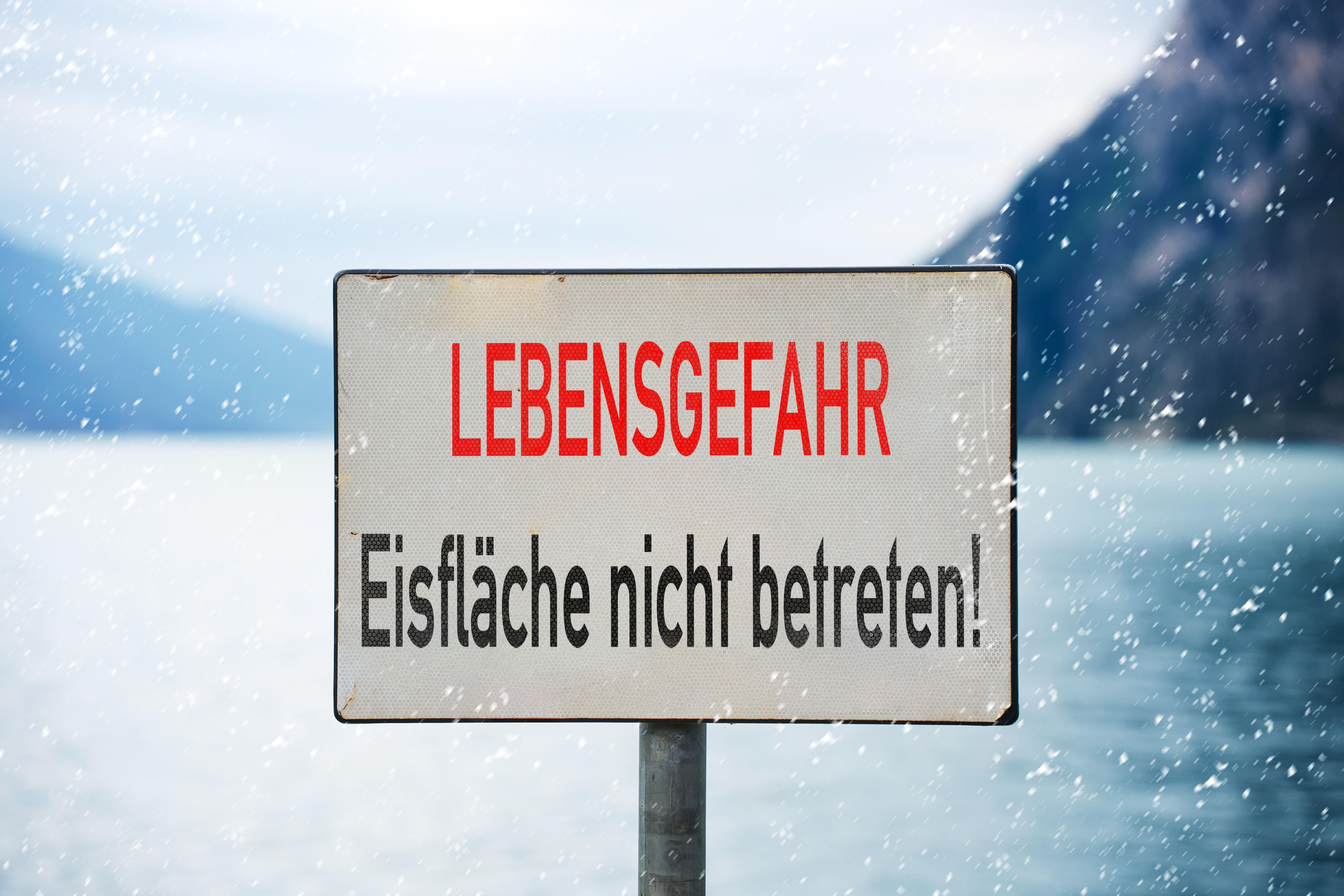 Ein Schild mit der Aufschrift: "Lebensgefahr: Eisfläche nicht betreten" vor winterlicher Kulisse