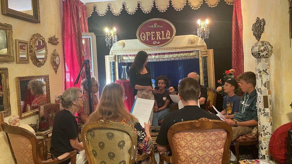 Mehrere Personen sitzen in einem Stuhlkreis und haben Textblätter in der Hand. 