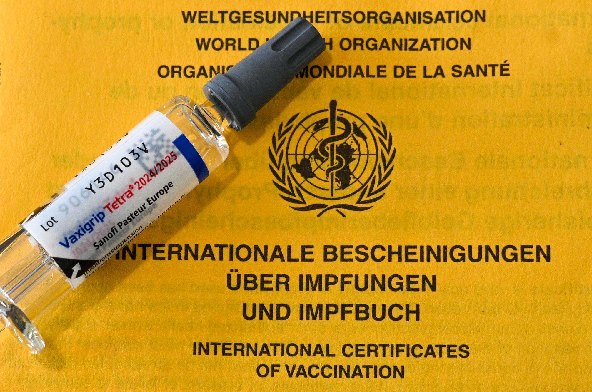 Eine Spritze mit Grippeimpfstoff liegt auf einem Impfpass