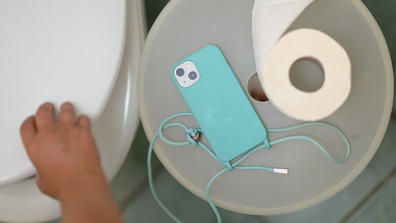Ein Smartphone und eine Klopapierrolle liegen neben einer Toilette auf einem Mülleimer. | Bild: picture alliance/dpa | Robert Michael Ein Smartphone und eine Klopapierrolle liegen neben einer Toilette auf einem Mülleimer.