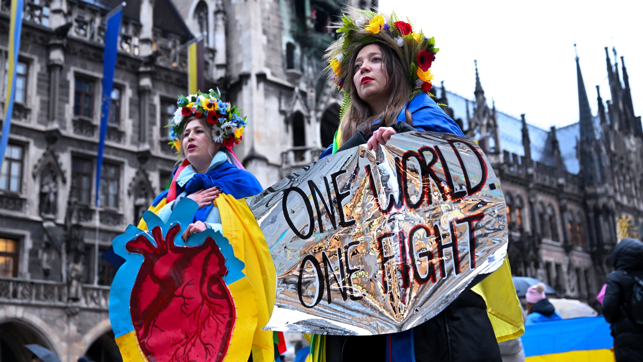 Zwei Frauen nehmen anlässlich des vierten Jahrestags des russischen Angriffs auf die Ukraine an einer Kundgebung auf dem Marienplatz teil und halten ein Plakat mit der Aufschrfit „One World - One Fight“ in den Händen.