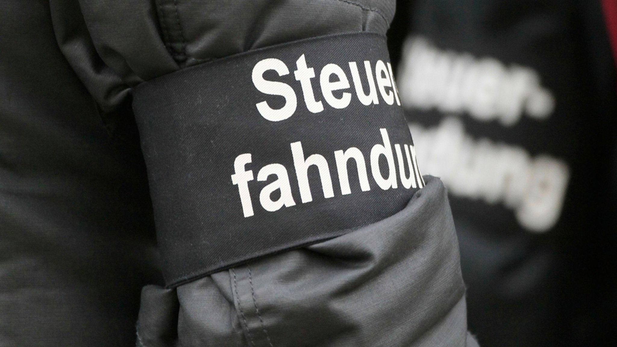 Der Arm eines Steuerfahnders - an ihm ist eine Armbinde mit der Aufschrift Steuerfahndung angebracht | Bild: dpa-Bildfunk/Sebastian Willnow Der Arm eines Steuerfahnders - an ihm ist eine Armbinde mit der Aufschrift Steuerfahndung angebracht
