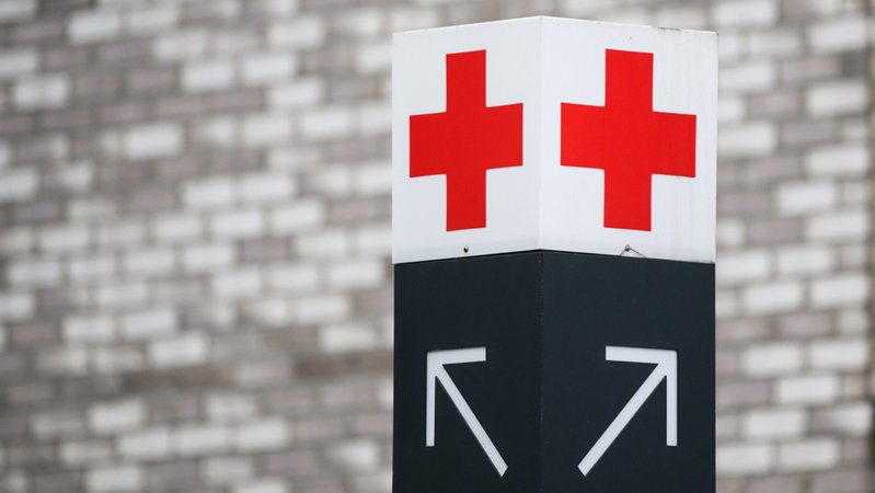 Ein Schild mit einem roten Kreuz weist den Weg zu einer Notaufnahme.