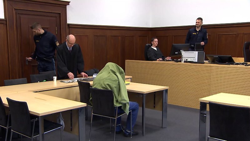 Angeklagter versteckt sich in Gerichtssaal unter seiner Jacke.