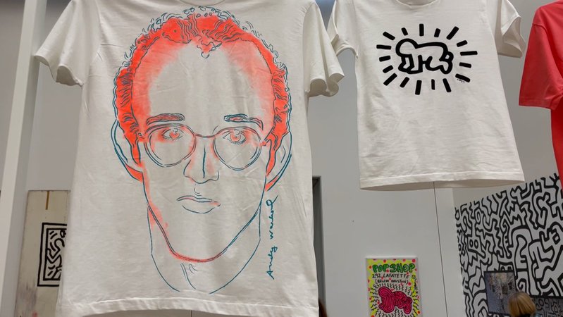 Zwei T-Shirts mit Bild von Warhol und einem Strichmännchen von Haring hängen von der Decke