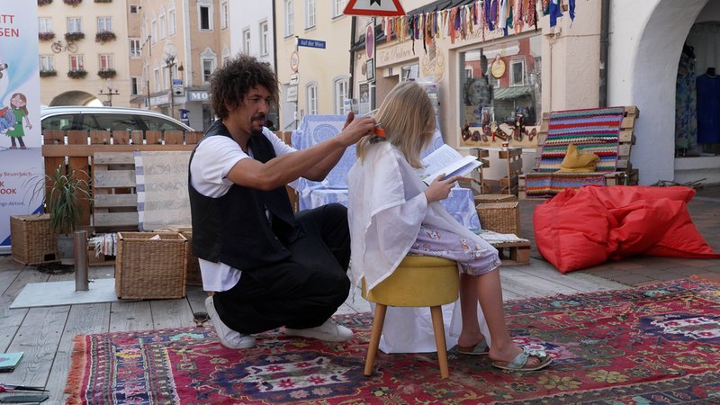 Der Friseur Danny Beuerbach schneidet einem Kind auf dem Mühlbacher Stadtplatz die Haare. | Bild: BR/Melina Eisemann Der Friseur Danny Beuerbach schneidet einem Kind auf dem Mühlbacher Stadtplatz die Haare.