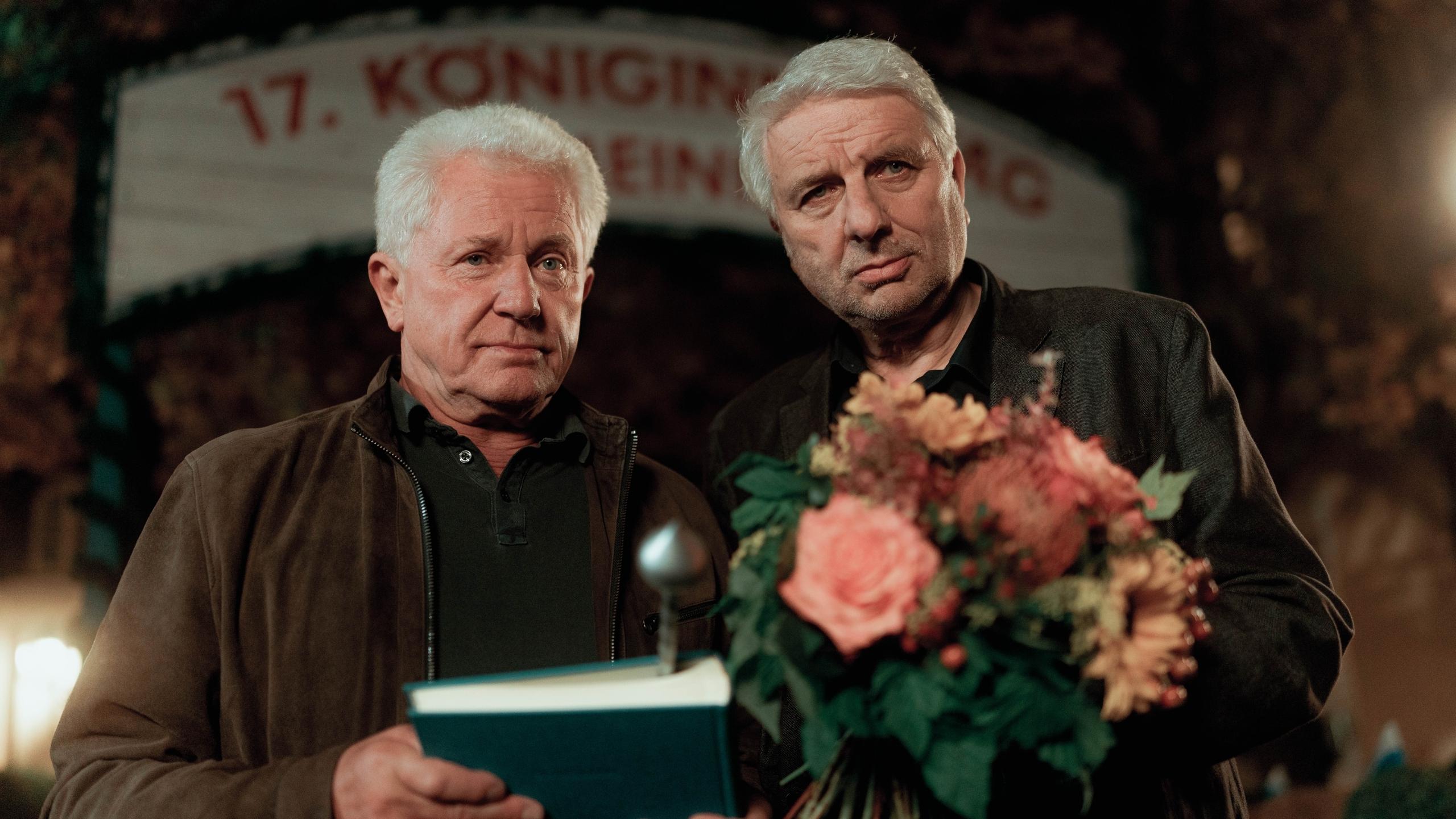 Szene aus dem "Tatort: Königinnen": Batic hält ein Buch in der Hand, Leitmayr einen Blumenstrauß.