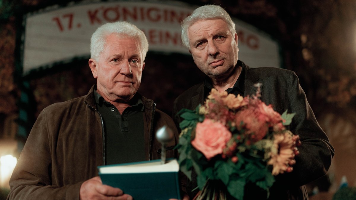 Szene aus dem "Tatort: Königinnen": Batic hält ein Buch in der Hand, Leitmayr einen Blumenstrauß.