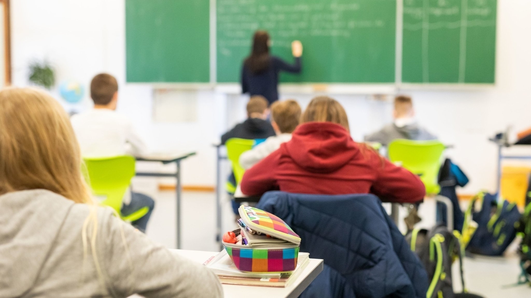 Schülerinnen und Schüler mit einer Lehrkraft im Klassenzimmer in einer Unterrichtssituation. (Symbolbild)