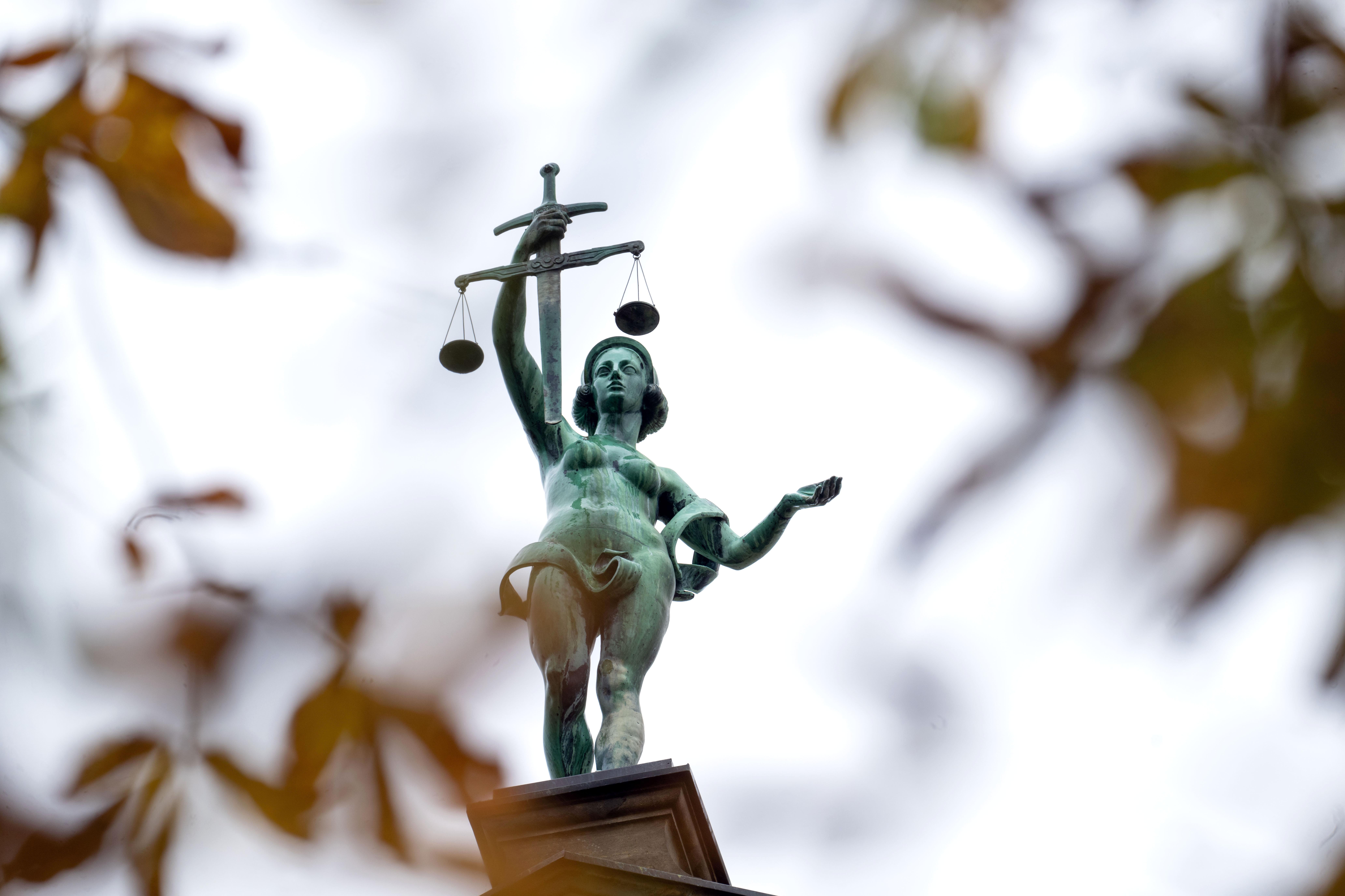 Hinter herbstlich verfärbten Blättern steht eine Statue der Justitia auf dem Gebäude des Landgerichts Bamberg.